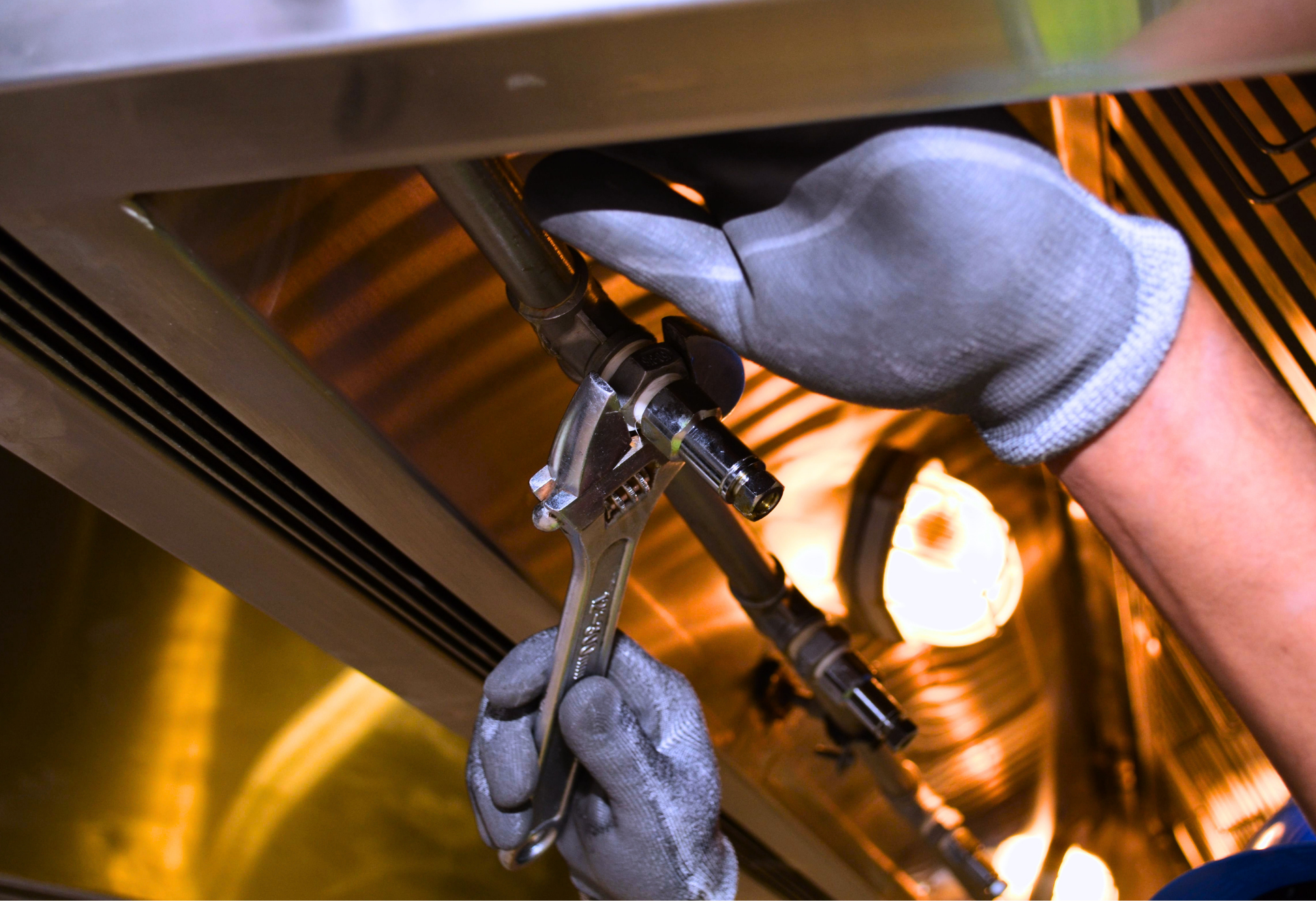 Macomb County plumber using an adjustable wrench to tighten a resident pipe fitting under a kitchen sink
